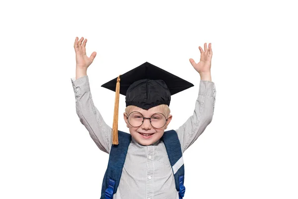 Retrato de um menino louro alegre em óculos grandes, chapéu acadêmico e uma bolsa de escola. Mãos para cima. Isolar — Fotografia de Stock