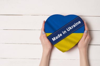 Yazıt Ukrayna, Ukrayna bayrağı made. Kalp şeklinde bir kutu tutan kadın elleri. Arka planda beyaz ahşap masa. Metin için yer