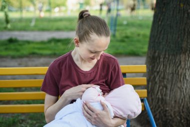 Kadın bir banktaki parkta bir bebeği emziriyor. Bahar günü