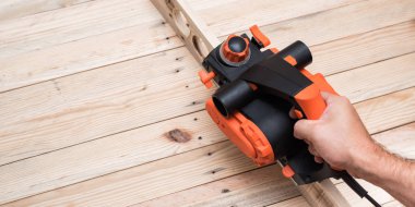 Erkek elinde elektrik planlayıcı. Açık kahverengi ahşap masa üzerinde iş parçası işleme.