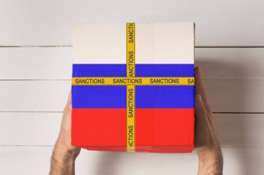 Sarı bant yazıtlı kutuda Rusya bayrağı erkek elinde yaptırımlar. Üstteki görünüm Arka planda beyaz tablo