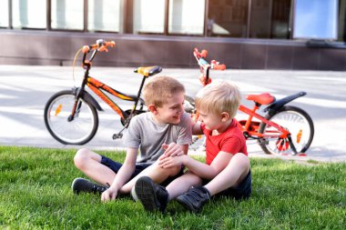 İki çocuk çimenlerin üzerinde otururken iletişim kuruyor. Bisikletten sonra dinlen, arka planda bisikletler