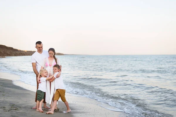 Familia feliz de cuatro abrazos en la costa del mar. Padres, madre embarazada y dos hijos . — Foto de Stock