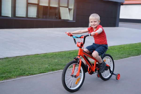 Beau garçon blond monte sur un vélo pour enfants. Contexte urbain — Photo