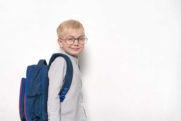 Retrato de um menino loiro de óculos e com uma mochila escolar em um fundo branco. Conceito escolar — Fotografia de Stock