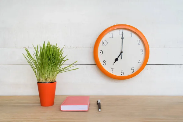 Круглий настінний годинник, рожевий блокнот на столі і зелений кімнатна рослина. Робоче місце. початок робочого дня — стокове фото