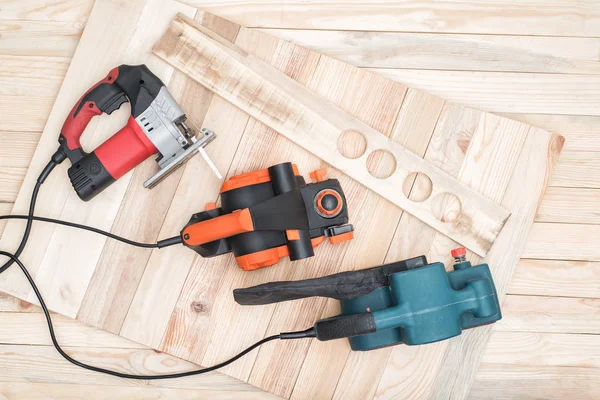 Set of handheld woodworking power tools for woodworking and the workpiece lies on a light wooden background. Directly above — Stock Photo, Image