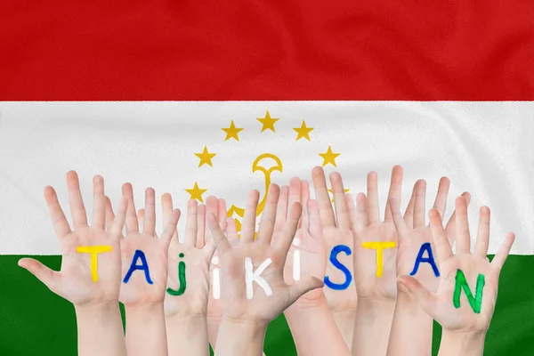 Επιγραφή Τατζικιστάν στα χέρια των παιδιών με φόντο τη σημαία του Τατζικιστάν — Φωτογραφία Αρχείου