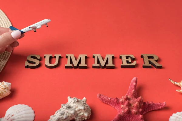 Pequeno avião na mão feminina. Palavra Verão de cartas de madeira. Conchas do mar, estrelas do mar e um fundo de coral vivo. Conceito de férias — Fotografia de Stock