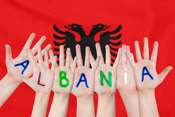 Inscripción Albania en las manos de los niños sobre el fondo de una bandera ondeante de Albania —  Fotos de Stock