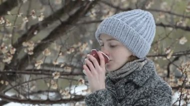 Kağıt bardaktan içen genç bir kadın. Çiçek açan yapraklar. Erken ilkbahar, karla karışık