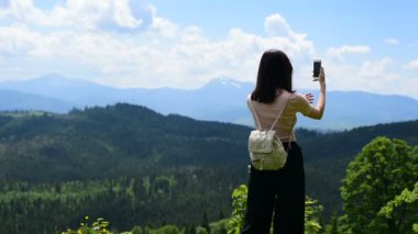 Dağ ve orman bir smartphone fotoğraf üzerinde bir sırt çantası ile kız. Arkadan görünüm. Güneşli yaz gün