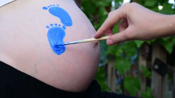 Kéz ecsettel felhívja a hasa kék baba lábnyom. Terhes koncepció. Közeli — Stock videók