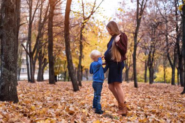 Küçük sarışın çocuk ve hamile annesinin karnı. Arka planda Sonbahar parkı