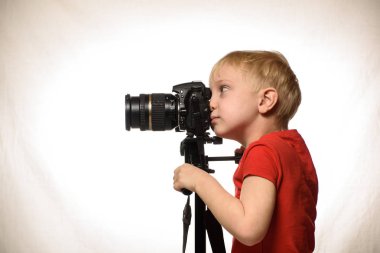 Sarışın çocuk bir Slr kamera ile fotoğraf çeker. Yan görünüm. Beyaz arka plan