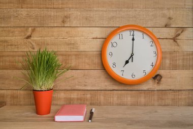 Kahverengi bir duvarda yuvarlak saat, yeşil bir ev bitkisi ve kalemli boş bir kağıt. İş planlama