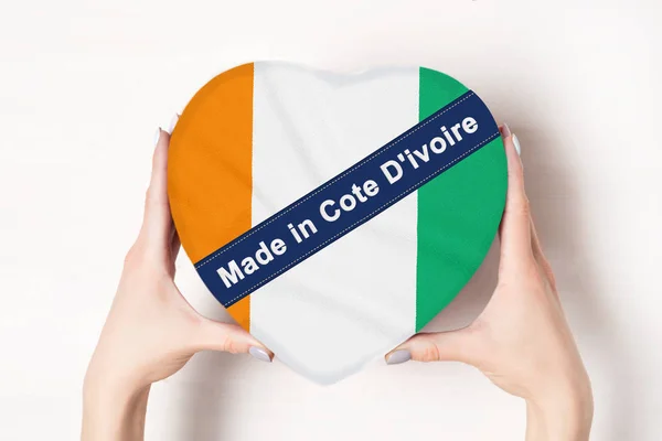 Felirat Made in Elefántcsontpart zászlaja Elefántcsontpart. Egy szív alakú dobozt tartó női kéz. Fehér háttér. — Stock Fotó