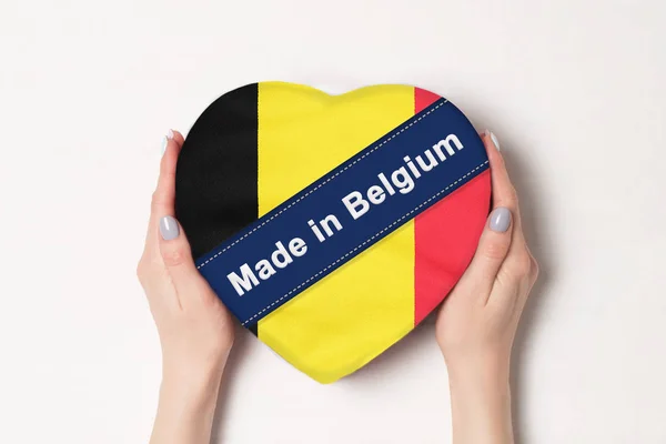 Επιγραφή Made in Βέλγιο, η σημαία του Βελγίου. Γυναικεία χέρια που κρατάνε ένα κουτί σε σχήμα καρδιάς. Λευκό φόντο. — Φωτογραφία Αρχείου