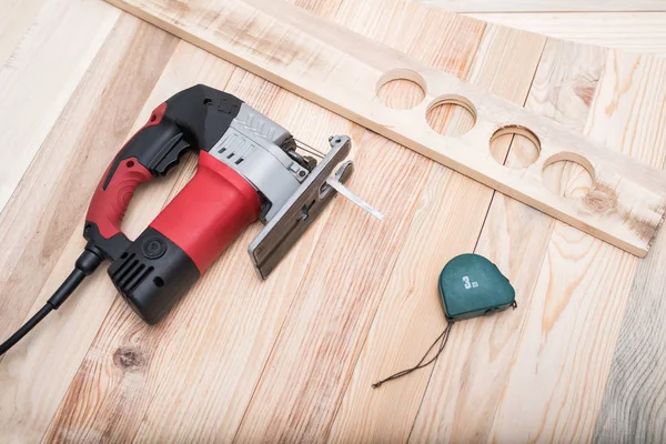 Elektrikli yapboz, ölçüm bandı ve iş parçası açık kahverengi ahşap bir masa üzerinde yatıyor. Ahşap. Yakın çekim