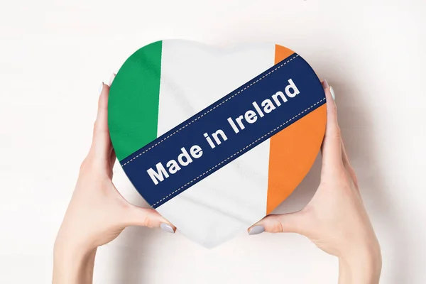 Felirata Made Írországban, Írország zászlója. Egy szív alakú dobozt tartó női kéz. Fehér háttér. — Stock Fotó