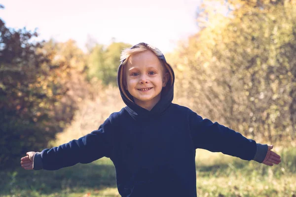 Sonriente chico rubio con los brazos abiertos en el capó. Preescolar. Día soleado — Foto de Stock