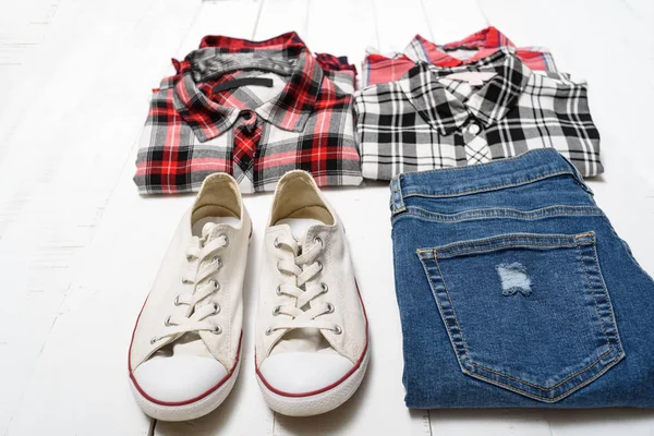 衣料品のコンセプト。白い木製の背景にチェック柄のシャツ、青いジーンズ、白いスニーカー. — ストック写真