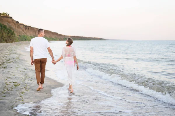 Casal jovem caminha mãos ao longo da costa do mar. Visão traseira — Fotografia de Stock