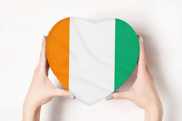 A CTE-divoire zászlaja a szív alakú dobozban egy női kezében. Fehér háttér — Stock Fotó