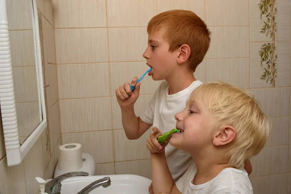 Dois rapazes escovam os dentes em frente a um espelho na casa de banho. Limpeza matinal — Fotografia de Stock