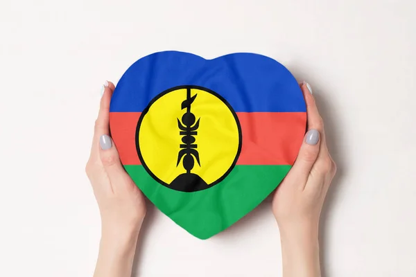 Σημαία της νέας Καληδονία σε ένα κουτί σε σχήμα καρδιάς σε γυναικεία χέρια. Λευκό φόντο — Φωτογραφία Αρχείου
