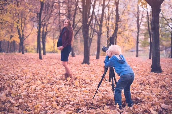 Mały blond chłopiec z dużym refleks kamery na statywie. Fotografa kobiety w ciąży. Sesja zdjęciowa rodzinna — Zdjęcie stockowe