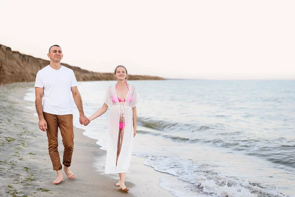 Jeune couple marié marche le long de la côte de la mer. Grossesse. Heure avant le coucher du soleil — Photo