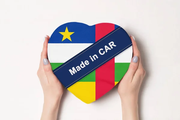 Inscrição Made in CAR, a bandeira da República Centro-Africana. Mãos femininas segurando uma caixa em forma de coração. Fundo branco . — Fotografia de Stock