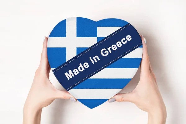 Inskriptionen är gjord i Grekland, Greklands flagga. Kvinnliga händer som håller en hjärtformad låda. Vit bakgrund. — Stockfoto