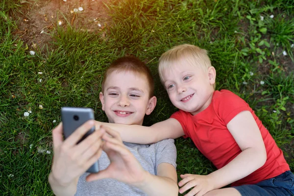 Çim üzerinde yatarken iki erkek bir smartphone üzerinde selfie yapmak. Üst görünüm