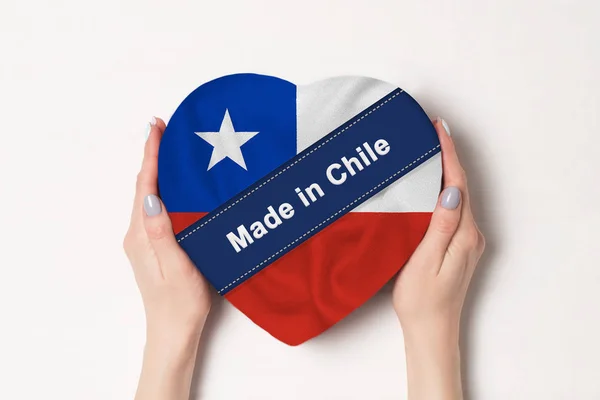 Inscriptie gemaakt in Chili de vlag van Chili. Vrouwelijke handen houden een hartvormige doos. Witte achtergrond. — Stockfoto