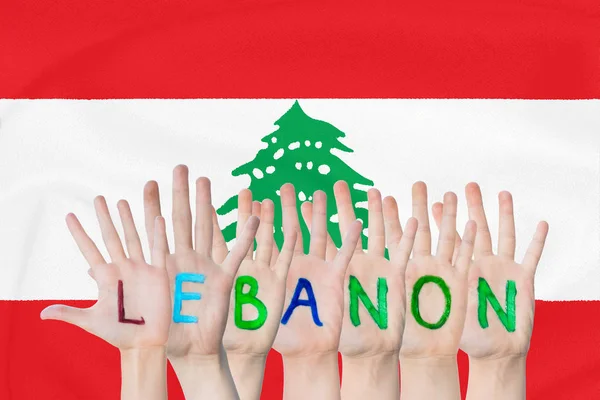 Inscripción Líbano en las manos de los niños sobre el fondo de una bandera ondeante del Líbano — Foto de Stock