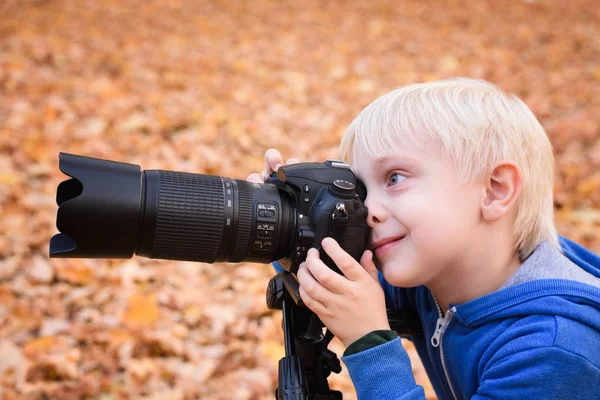 Portrét malého blonďáku fotografuje na SLR kameře. Podzimní Park — Stock fotografie