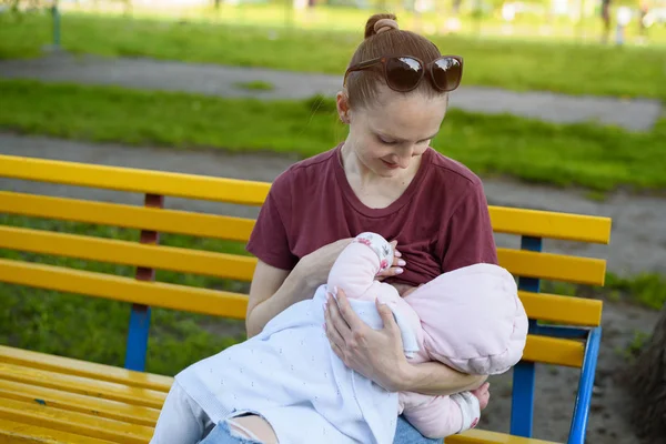 Woman is breastfeeding a baby in a park on a bench. Spring day — Stock Photo, Image
