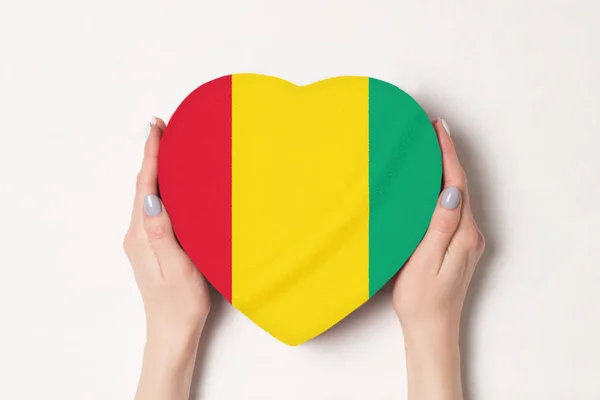 Bandeira da Guiné em uma caixa em forma de coração em mãos femininas. Fundo branco — Fotografia de Stock