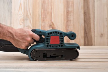 Elektrikli kemer zıpkın, erkek elinde zıpzAma makinesi. Açık kahverengi ahşap masa üzerinde iş parçası işleme. Yan görünüm, yakın