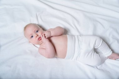 Beyaz çarşaflar üzerinde yatan çıplak bir gövde ile sevimli sarışın bebek. Üstte görüntü