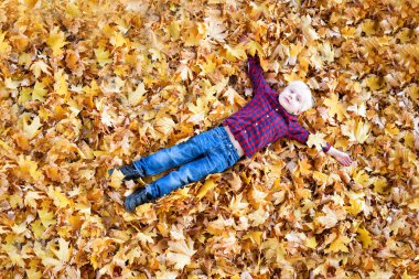 Bir ekose gömlek sarışın çocuk sarı sonbahar yaprakları yatıyor. Üst görünüm. Sonbahar konsepti