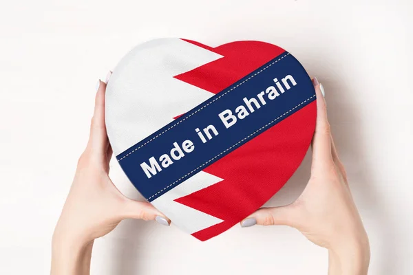 Επιγραφή Made in Μπαχρέιν η σημαία του Μπαχρέιν. Γυναικεία χέρια που κρατάνε ένα κουτί σε σχήμα καρδιάς. Λευκό φόντο. — Φωτογραφία Αρχείου