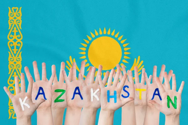 Inscription Kazakhstan sur les mains des enfants sur le fond d'un drapeau agitant du Kazakhstan — Photo