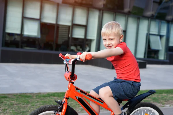 Beau garçon blond monte sur un vélo pour enfants. Contexte urbain — Photo