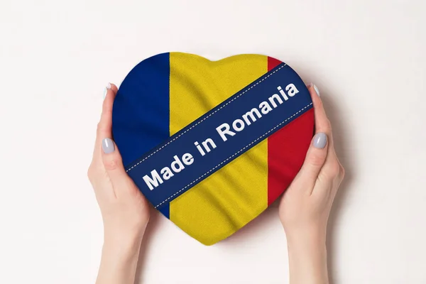Επιγραφή Made in Ρουμανία η σημαία της Ρουμανίας. Γυναικεία χέρια που κρατάνε ένα κουτί σε σχήμα καρδιάς. Λευκό φόντο. — Φωτογραφία Αρχείου