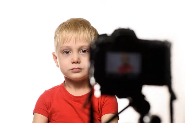 Serieuze blonde jongen is het opnemen van een video op DSLR camera. Kleine videoblogger. Witte achtergrond — Stockfoto