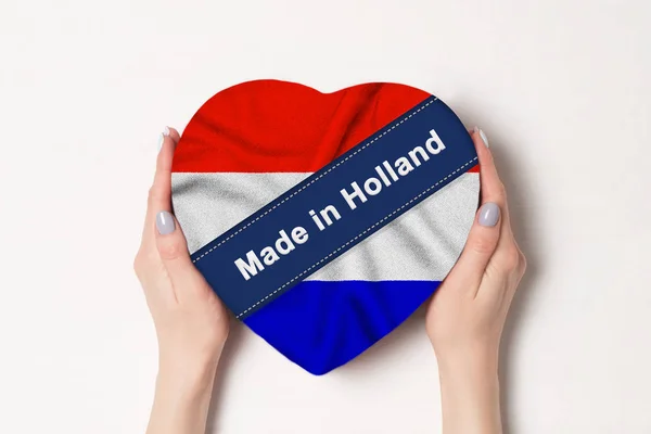 Επιγραφή φτιαγμένο στην Ολλανδία, η σημαία της Ολλανδίας. Γυναικεία χέρια που κρατάνε ένα κουτί σε σχήμα καρδιάς. Λευκό φόντο. — Φωτογραφία Αρχείου