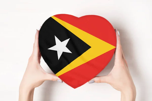 Bandera de Timor Oriental en una caja con forma de corazón en manos femeninas. Fondo blanco — Foto de Stock